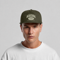 A man wearing an olive green flat-brim cap with 'ARENA STEREO' printed in cream on the front, paired with a white crewneck t-shirt, set against a plain light gray background.