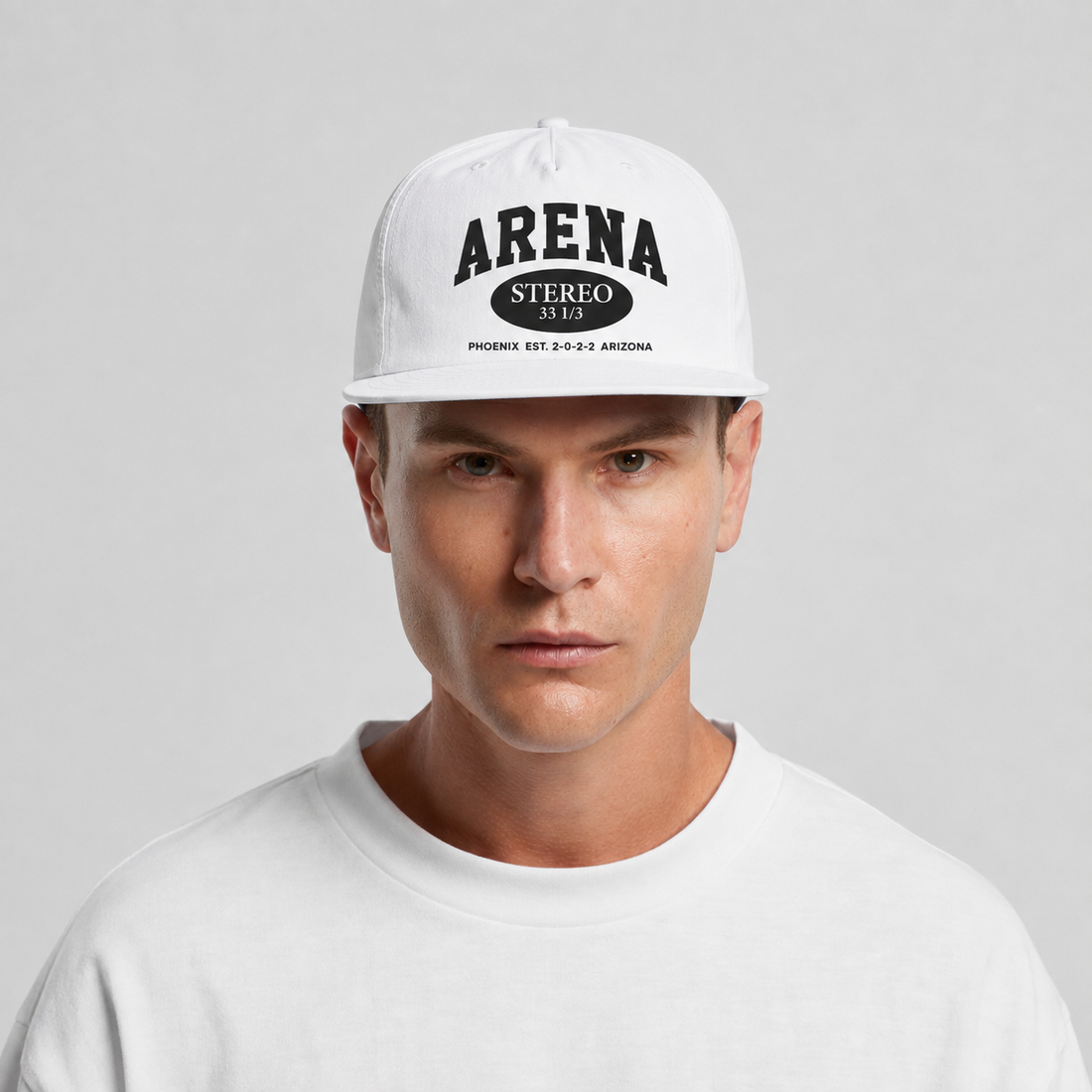 A man wearing a white surf cap with black text reading 'ARENA STEREO' and a white crewneck shirt, photographed against a light gray studio background.