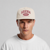 A man wearing a bone-colored surf cap with a rose 'ARENA' graphic on the front, paired with a white t-shirt against a light gray background.