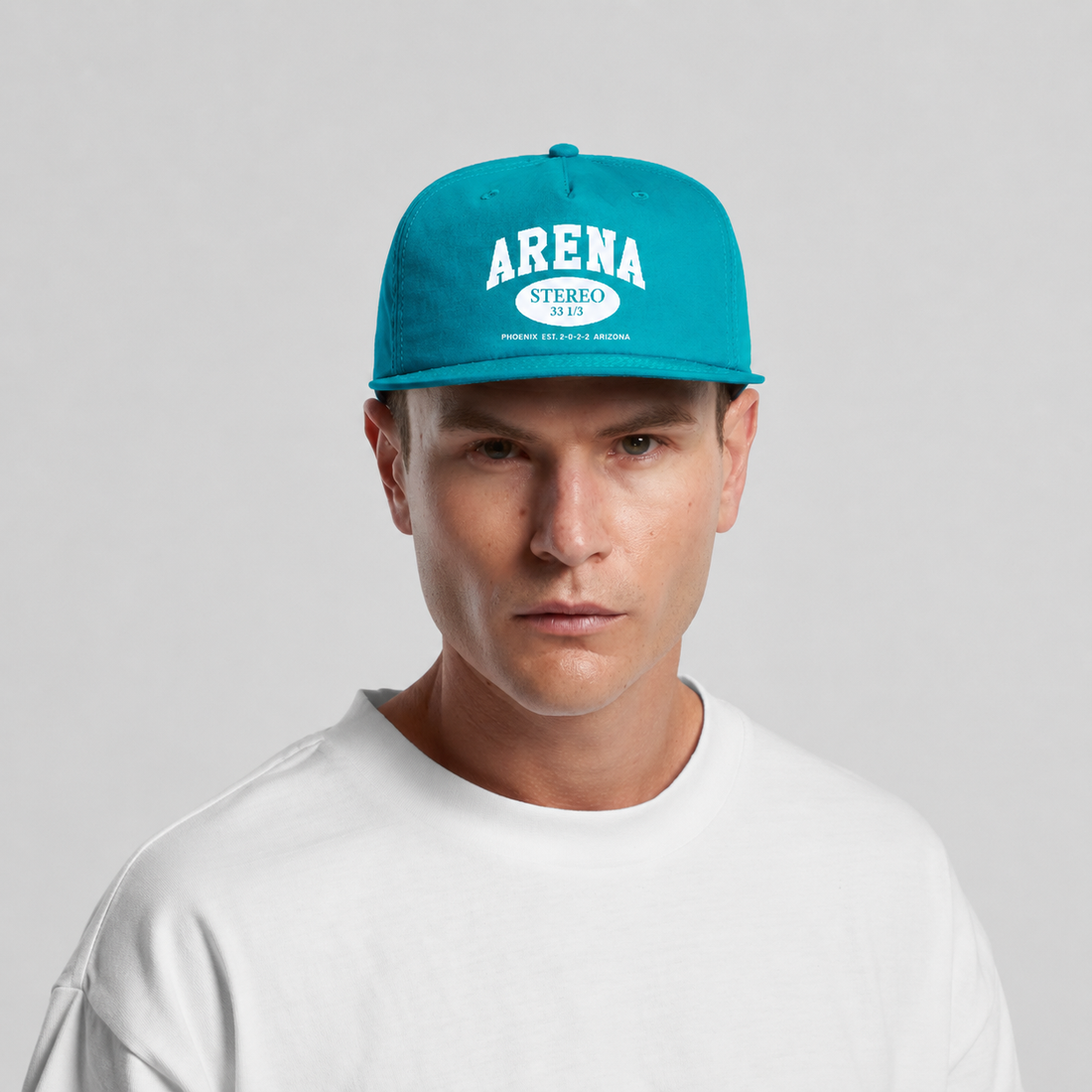 A man wearing a bright turquoise snapback cap with white 'ARENA' text on the front, paired with a white t-shirt against a light gray background.
