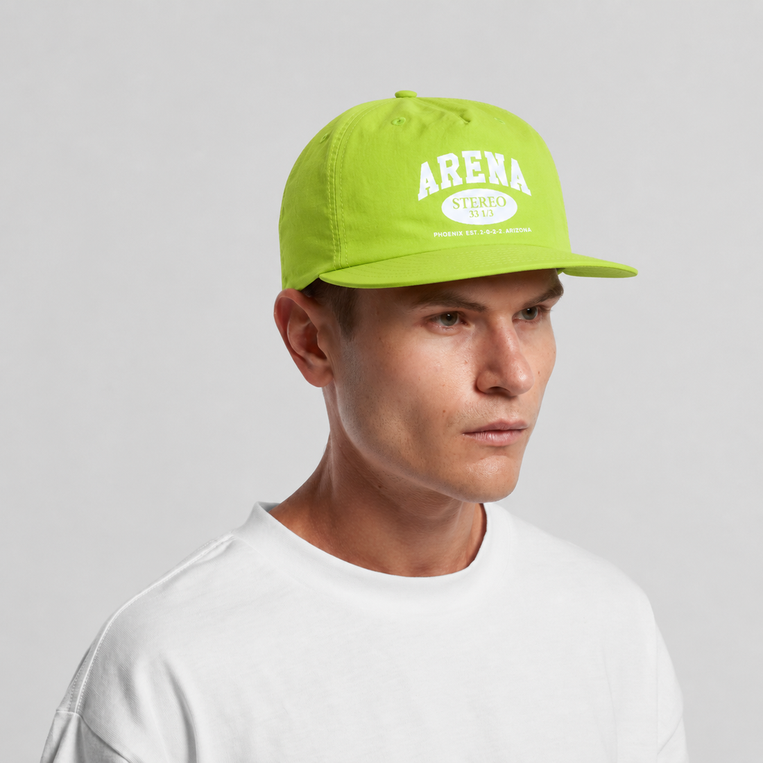 A man wearing a citrus green flat-brim cap with 'ARENA STEREO' printed in white on the front, paired with a white crewneck t-shirt, set against a plain light gray background.