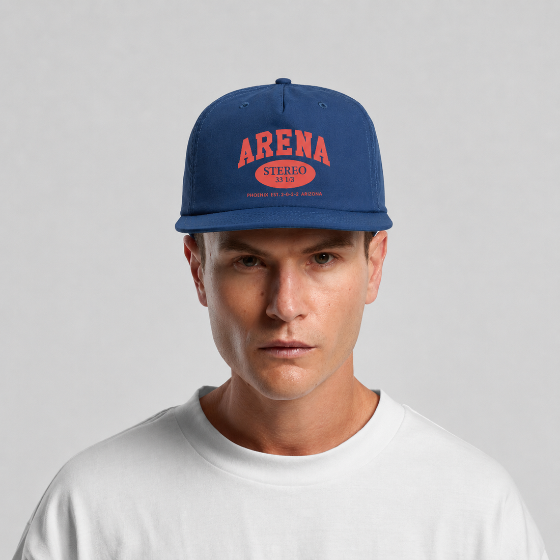 A man wearing a blue snapback cap with red and orange 'ARENA STEREO' text on the front, paired with a white t-shirt, against a light gray background.