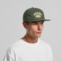A man wearing a cypress green flat-brim cap with 'ARENA STEREO' printed in cream on the front, paired with a white crewneck t-shirt, set against a plain light gray background.