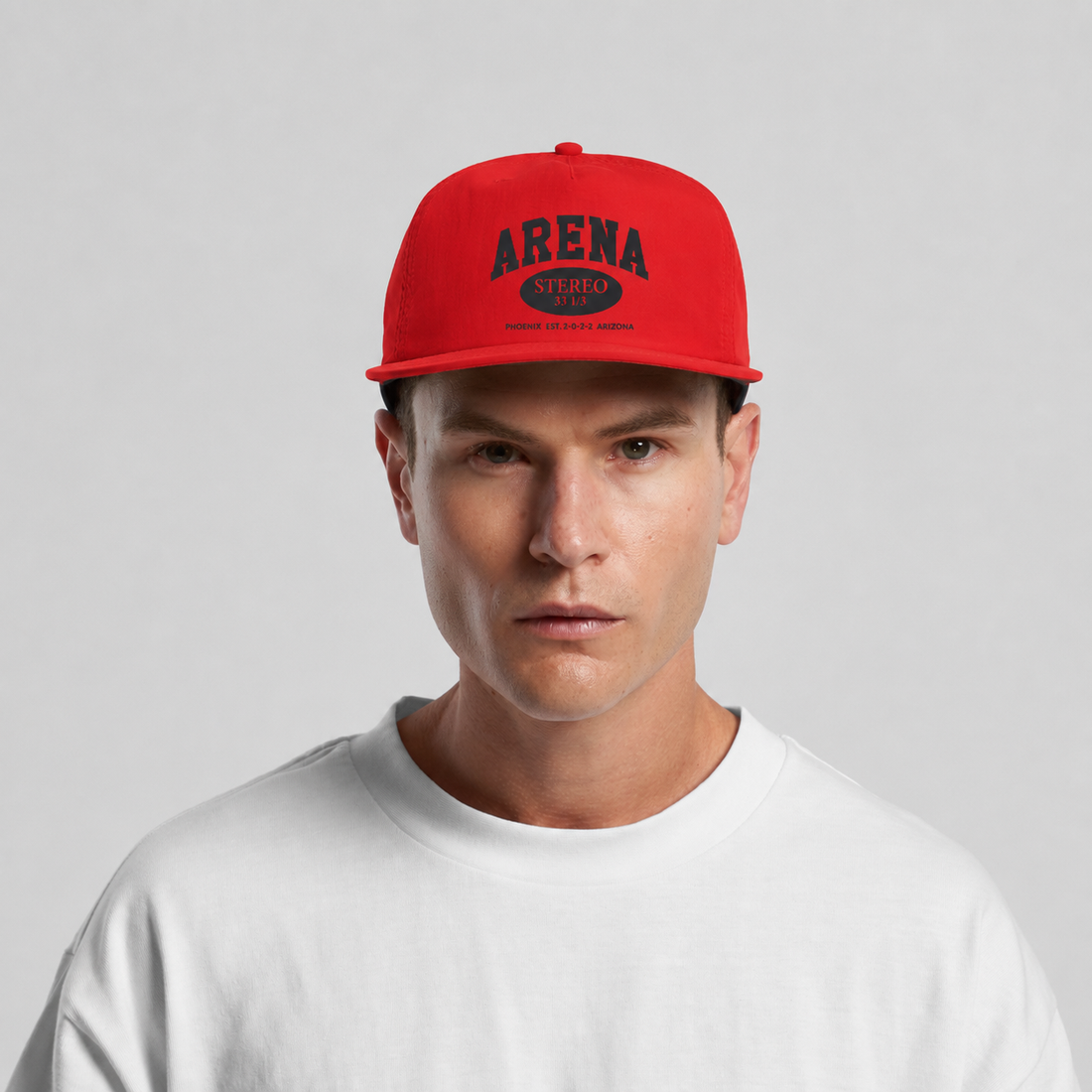 A man wearing a bright red snapback cap with 'ARENA' printed in black on the front, paired with a white crewneck t-shirt against a light gray background.