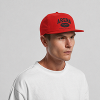 A man wearing a red snapback cap with 'ARENA STEREO' printed in black on the front, paired with a white crewneck t-shirt against a light gray studio background.
