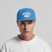 A man wearing a bright blue snapback cap with 'ARENA STEREO' printed in white on the front, paired with a white t-shirt against a light gray background.