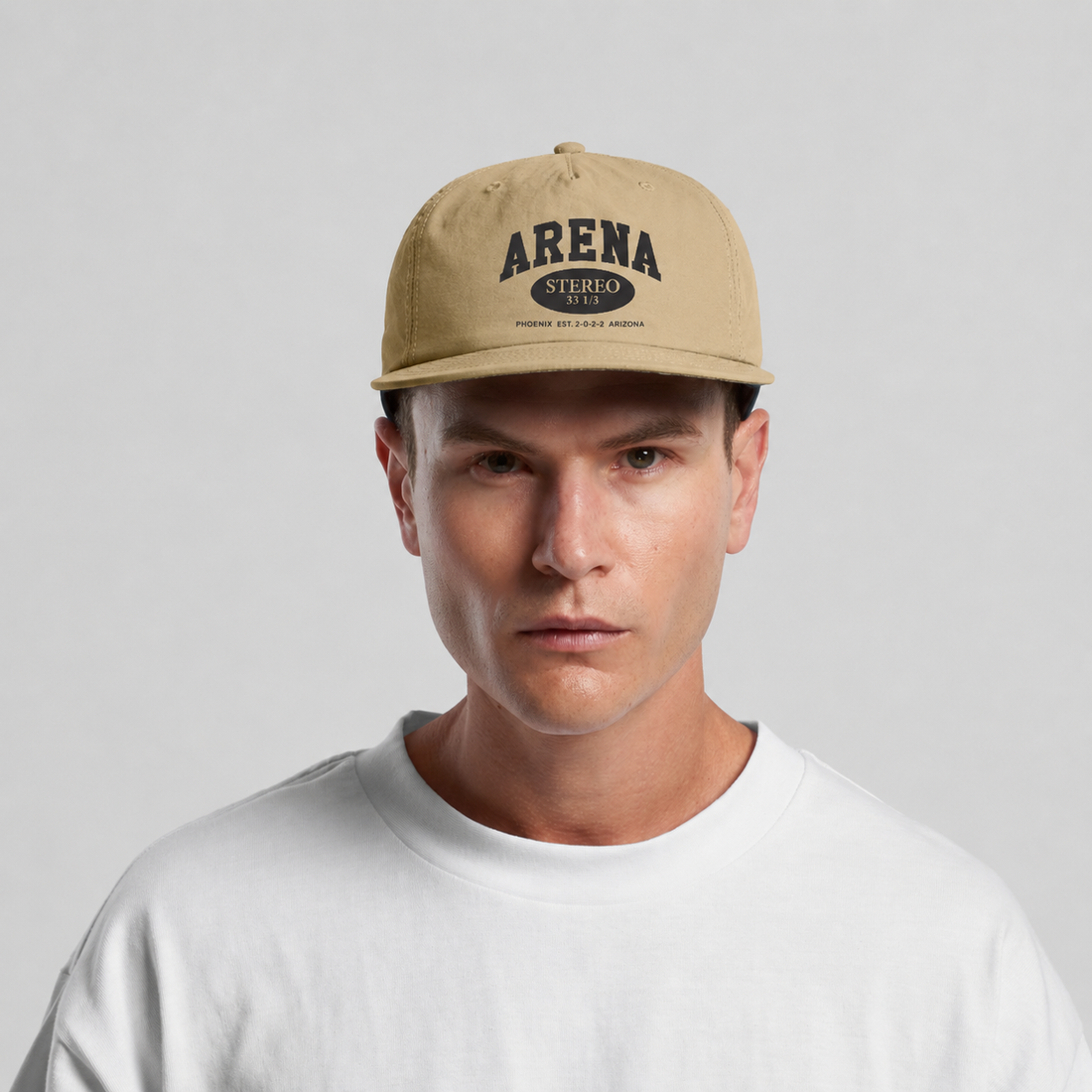 A man wearing a beige snapback cap with 'ARENA STEREO' printed in black on the front, paired with a white t-shirt, against a light gray background.