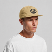 A man wearing a beige snapback cap with 'ARENA' printed in black on the front, paired with a white t-shirt, photographed against a neutral light gray background.
