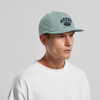 A man wearing a light sage green baseball cap with 'ARENA' printed in black on the front, paired with a white crewneck t-shirt, against a neutral gray background.