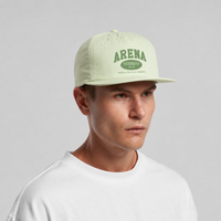 A man wearing a light sage green snapback cap with a dark green 'ARENA STEREO' logo on the front, paired with a white t-shirt against a neutral gray background.
