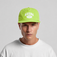 A man wearing a bright green flat-brim surf cap with white 'ARENA STERFO' text on the front, paired with a white crewneck t-shirt, against a light gray studio background.