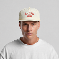 A man wearing a cream-colored Arena Stereo surf cap and a white t-shirt, photographed against a neutral light gray background.