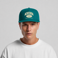 A man wearing a teal green snapback cap with cream-colored 'ARENA STEREO' text on the front, paired with a white t-shirt against a light gray background.