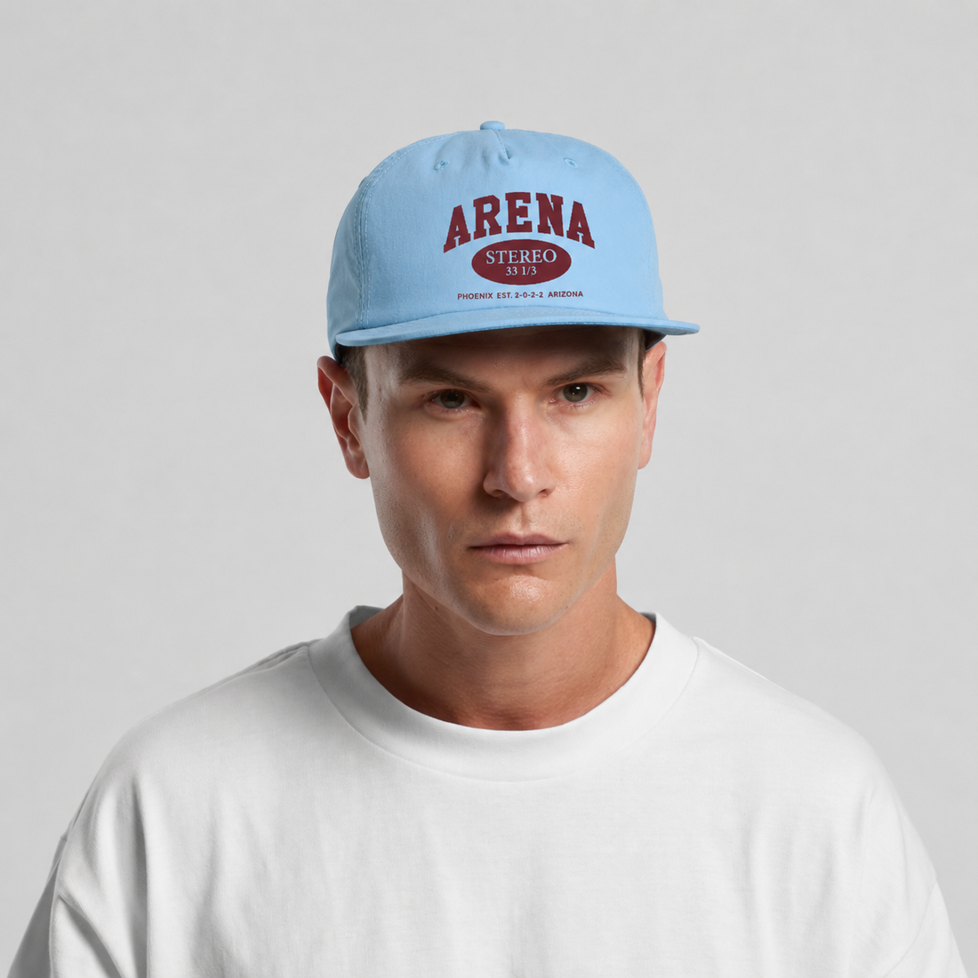 A man wearing a light blue snapback cap with 'ARENA' printed in red on the front, paired with a white t-shirt against a light gray background.