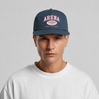 A man wearing a navy blue snapback cap with pink 'ARENA STEREO' text on the front, paired with a white t-shirt against a light gray background.