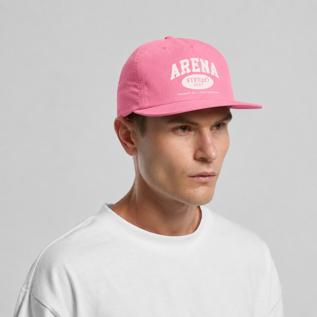 A man wearing a pink baseball cap with 'ARENA' printed in white on the front, paired with a white t-shirt, against a light gray studio background.