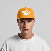 A man wearing a mustard yellow snapback cap with 'ARENA STEREO 2022' printed in white on the front, paired with a white t-shirt, against a light gray background.
