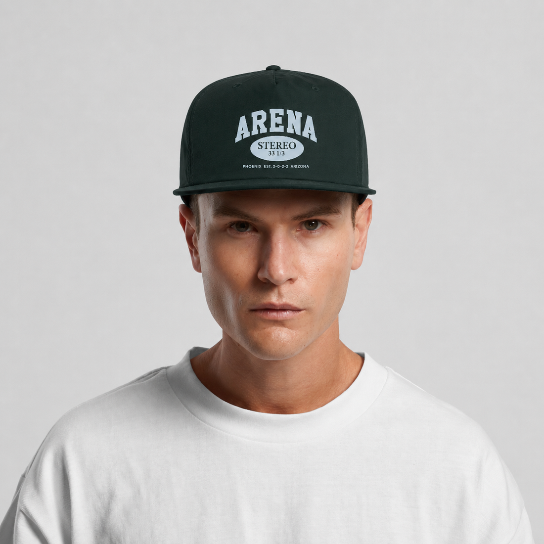 A man wearing a dark green snapback cap with 'ARENA STEREO 33 1/3' printed in white on the front, paired with a white t-shirt against a light gray background.