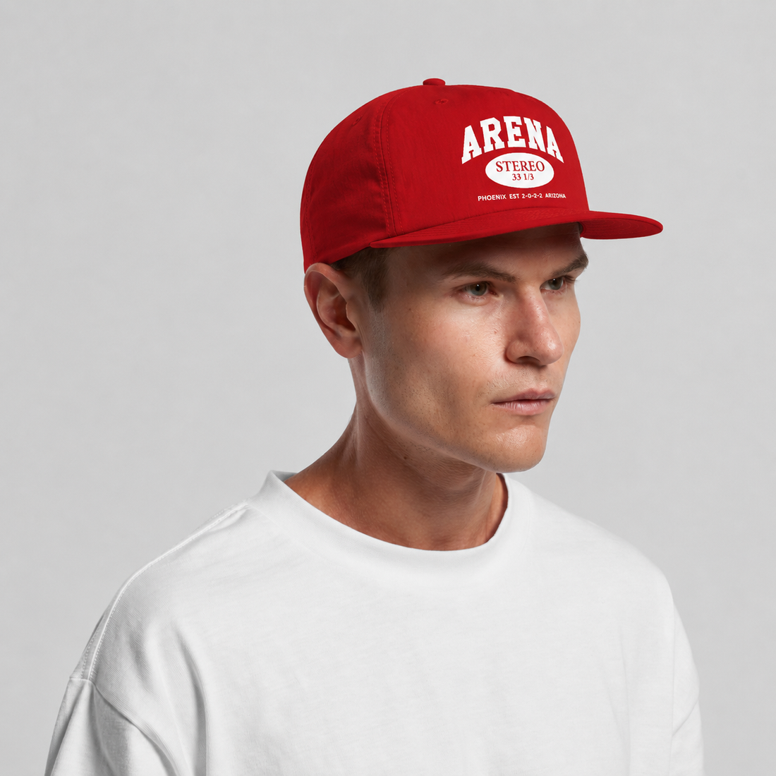 A man wearing a red snapback cap with 'ARENA STEREO' printed in white on the front, paired with a white t-shirt, set against a plain light gray background.