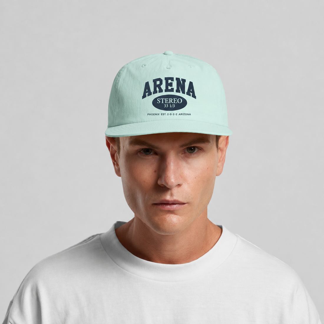 A man wearing a light mint green snapback cap with 'ARENA STEREO WY' printed in dark navy blue on the front, paired with a white t-shirt against a neutral gray background.