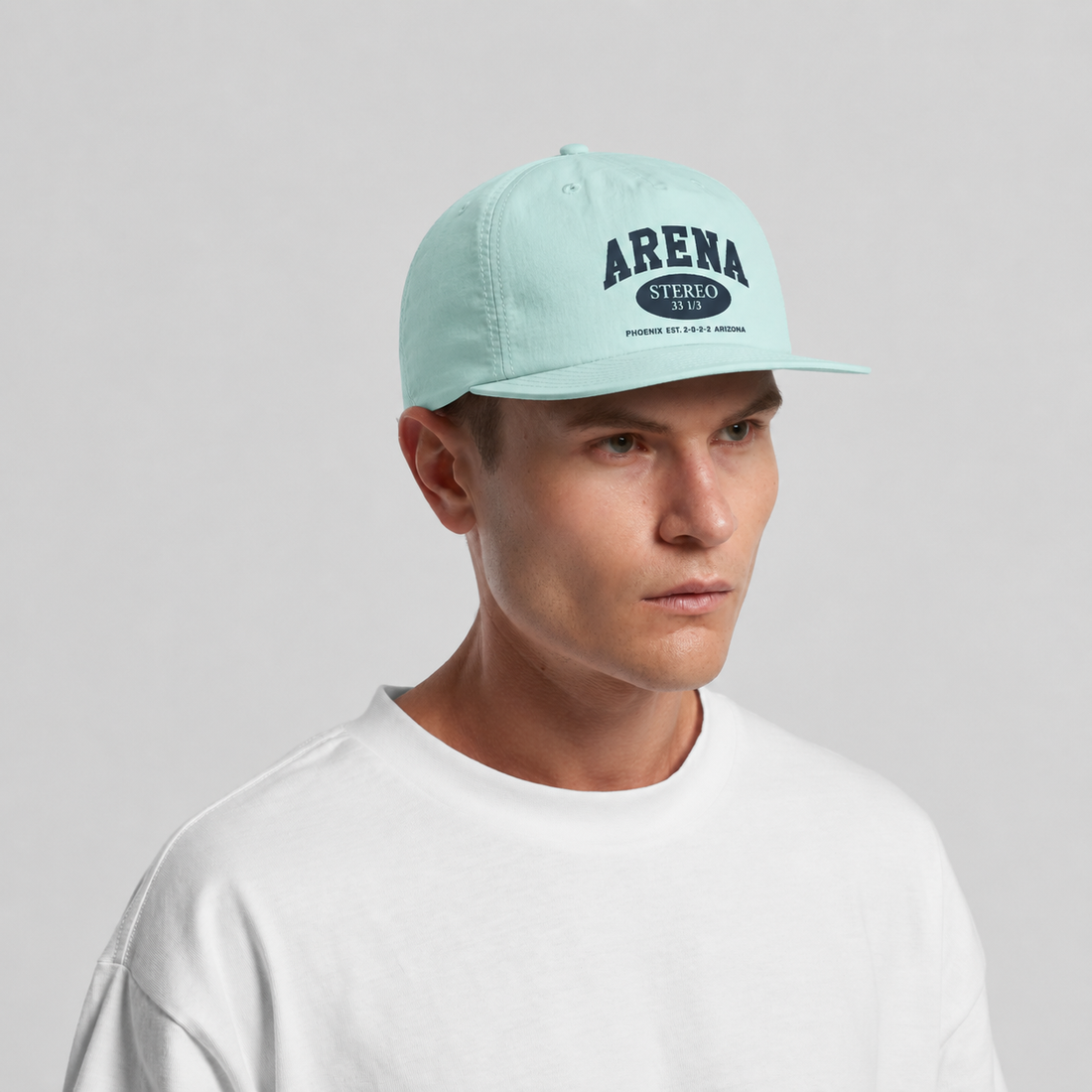 A man wearing a light mint green Arena snapback cap and a white t-shirt, photographed against a neutral light gray background.