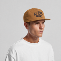 A man wearing a tan snapback cap with 'ARENA STEREO' printed in black on the front, paired with a white crewneck t-shirt, against a light gray background.