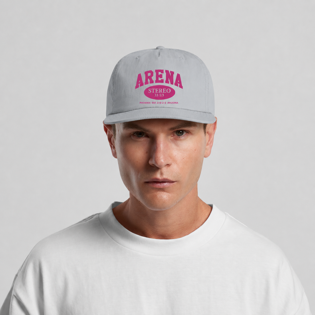 A man wearing a light gray snapback cap with a pink 'ARENA STEREO' graphic on the front, paired with a white t-shirt, against a light gray background.