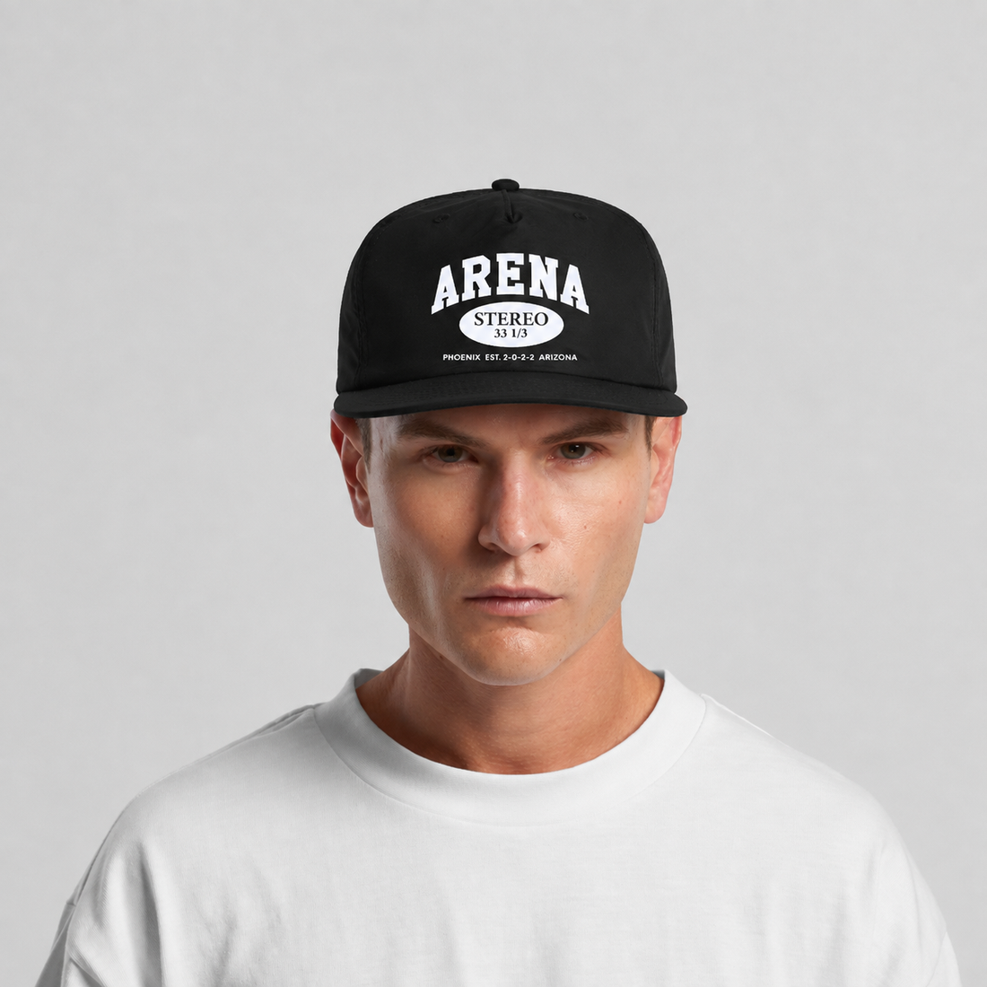 A man wearing a black snapback cap with a white graphic logo that reads 'ARENA STEREO' on the front, paired with a white crewneck t-shirt against a light gray background.