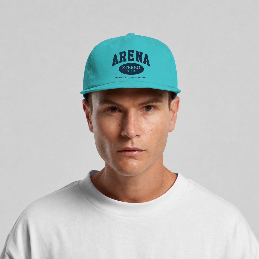 A man wearing a bright turquoise blue snapback cap with 'ARENA STEREO 501' printed in dark blue on the front, paired with a white crewneck t-shirt against a light gray background.