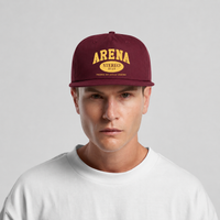A man wearing a maroon snapback cap with yellow embroidered text reading 'ARENA STEREO' and a white crewneck t-shirt, photographed against a light gray studio background.