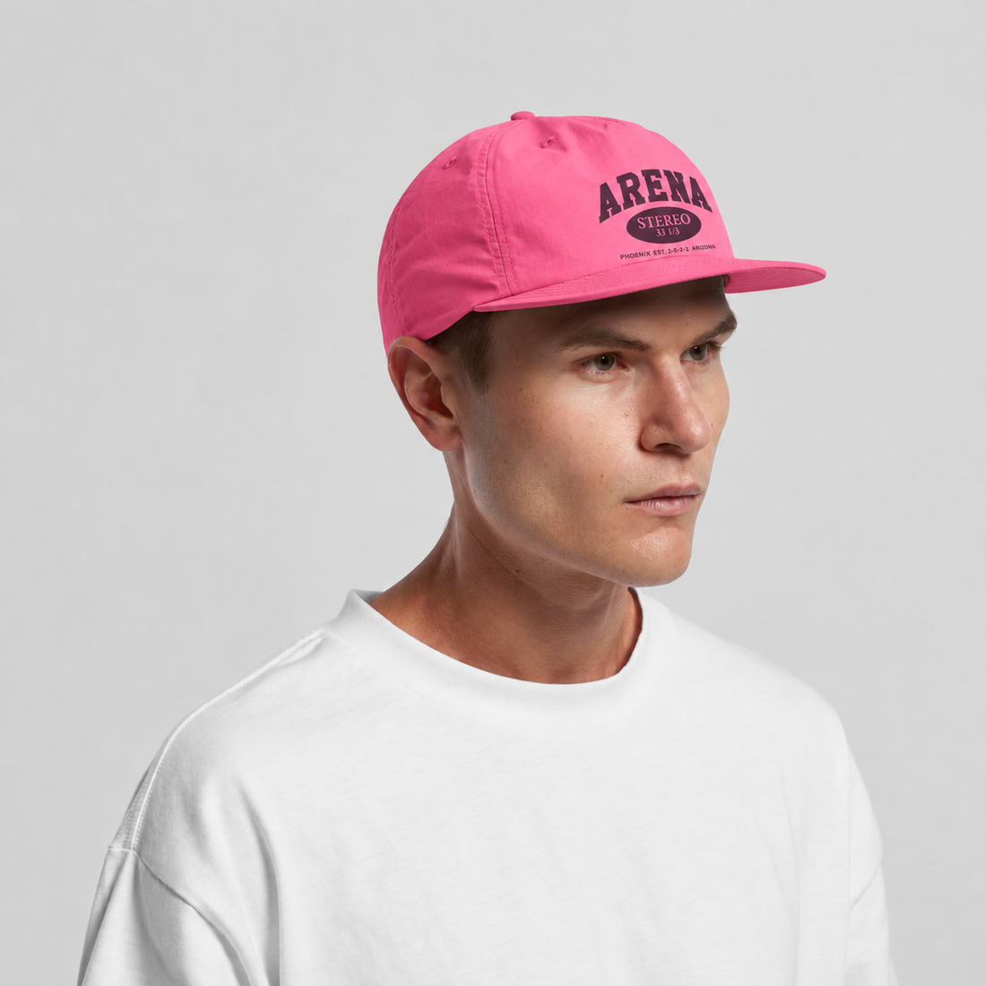 A man wearing a bright pink baseball cap with 'ARENA' printed in dark pink on the front, paired with a white crewneck sweatshirt against a light gray background.