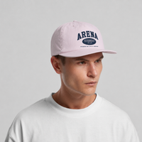 A man wearing a orchid pink baseball cap with navy blue 'ARENA STEREO' text on the front, paired with a white crewneck t-shirt, against a solid light gray background.