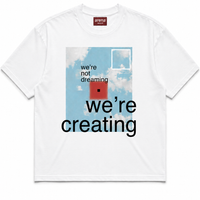 A white crewneck t-shirt featuring a graphic print on the front. The graphic depicts a light blue sky with white clouds, a red square, and black text reading 'we're not dreaming we're creating'.