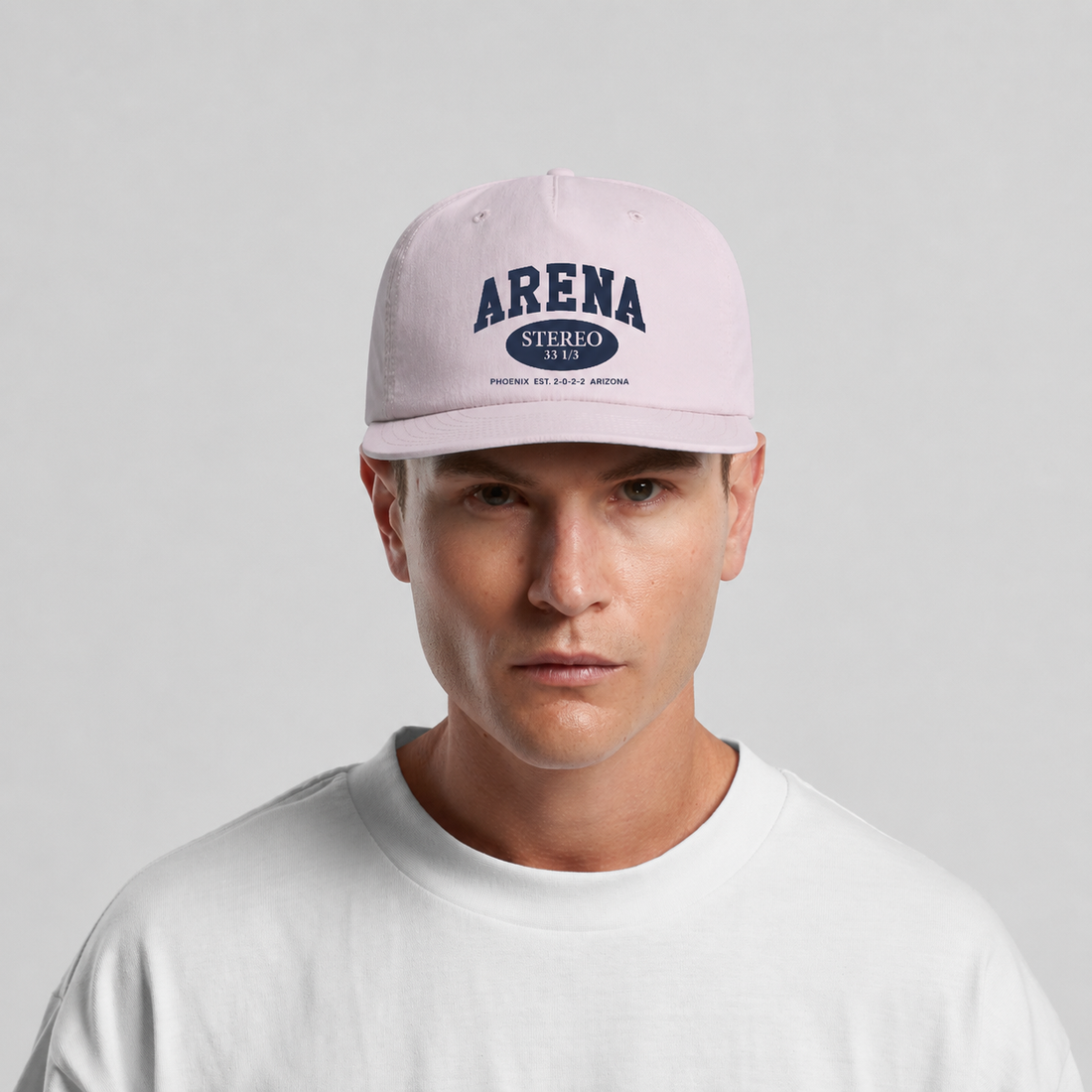 A man wearing a orchid pink surf cap with navy blue 'ARENA' text on the front, paired with a white t-shirt against a neutral gray background.